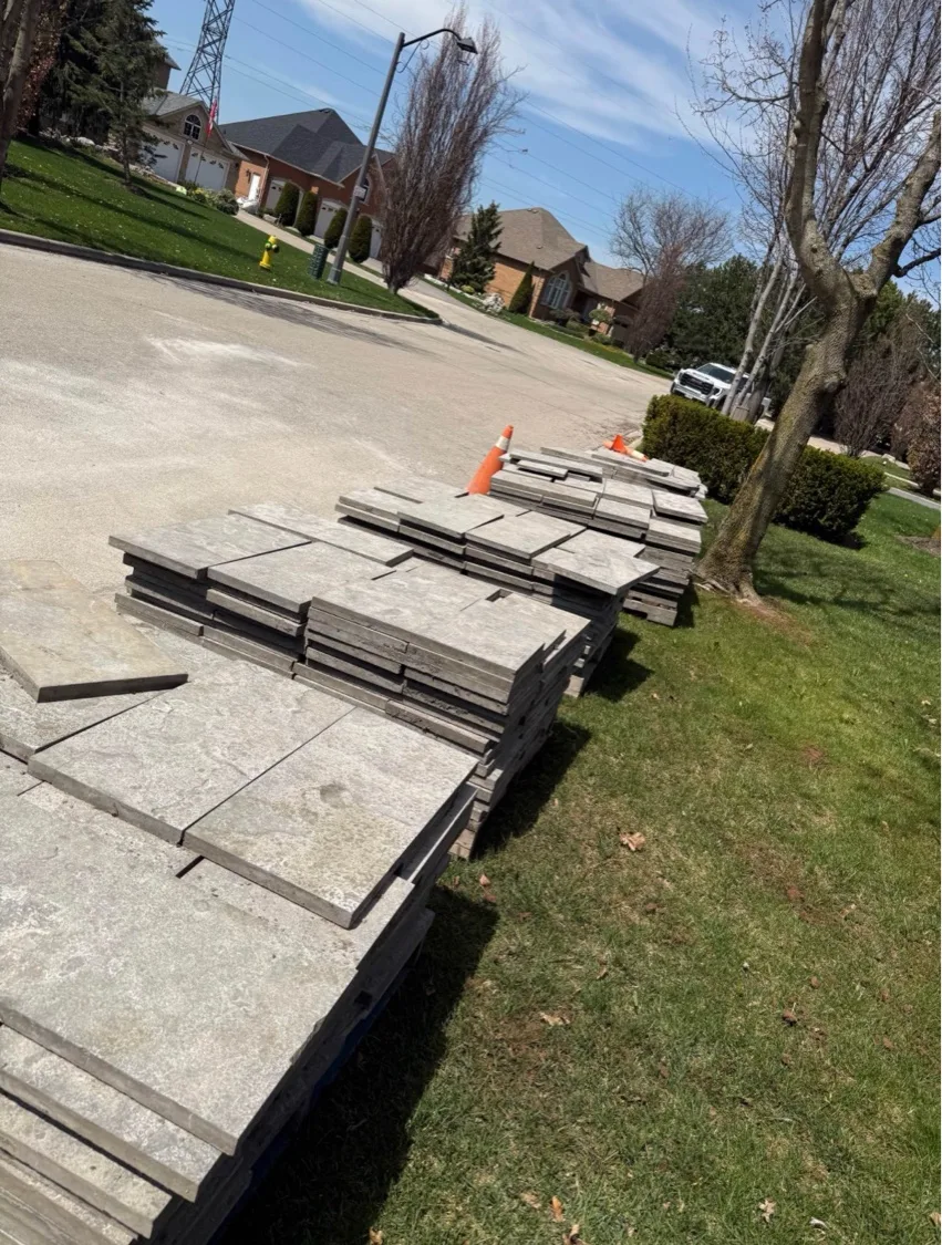 Pallets of natural grey stone slabs staged curbside in residential Kitchener-Waterloo neighbourhood ready for interlock install — D&D Exterior Finishing