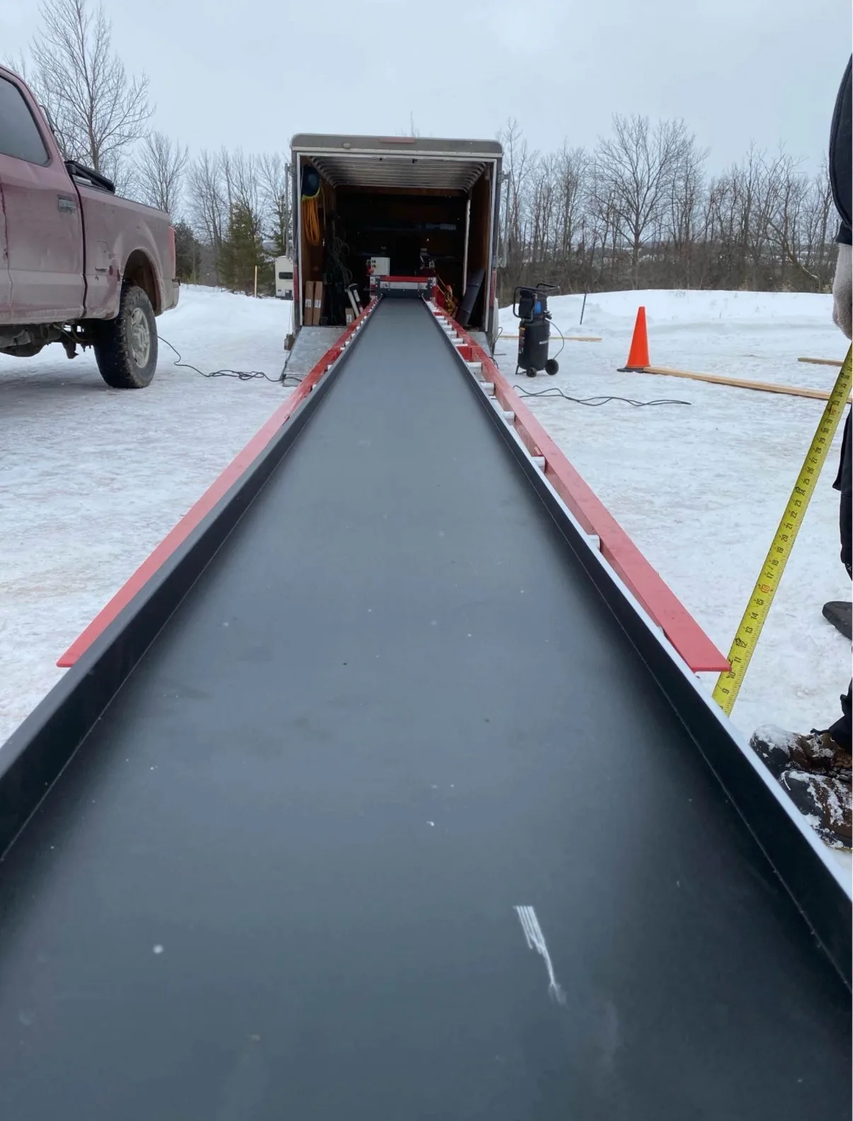 Long custom-formed black metal roof panel extruded on-site from trailer-mounted forming machine — D&D Exterior Finishing
