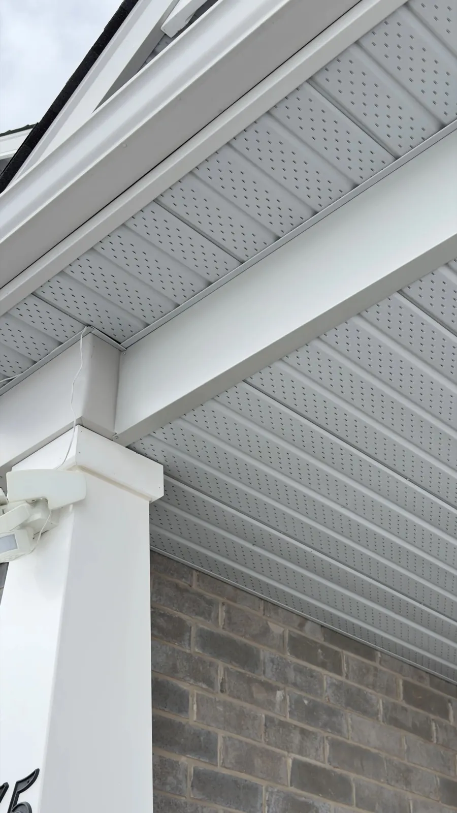 Perforated white soffit beside fascia and a brick wall