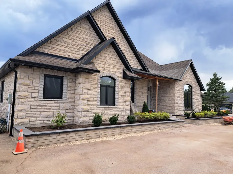 Stone-clad house with dark gables, white roofline trim and a paved approach