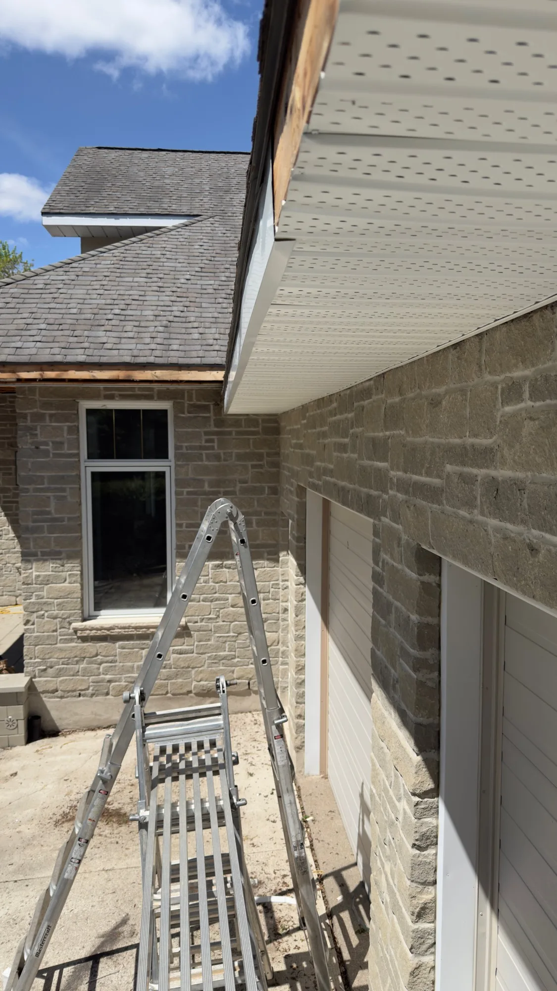 Vented soffit install in progress with exposed treated wood substrate above stone home garage